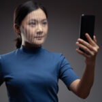 Asian woman scans face by smart phone using facial recognition system. Isolated on background.