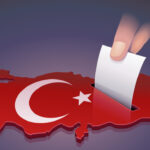 Hand dropping a ballot into a slot on the 3D map of Turkey in the colors of the Turkish flag symbolizing an election in Turkey on dark background
