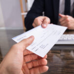 Close-up Of A Businessperson's Hand Giving Cheque To Colleague At Workplace