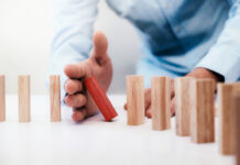 Businessman hand stop dominoes continuous toppled or risk with copyspace. Business risk, strategy and planing concept idea.