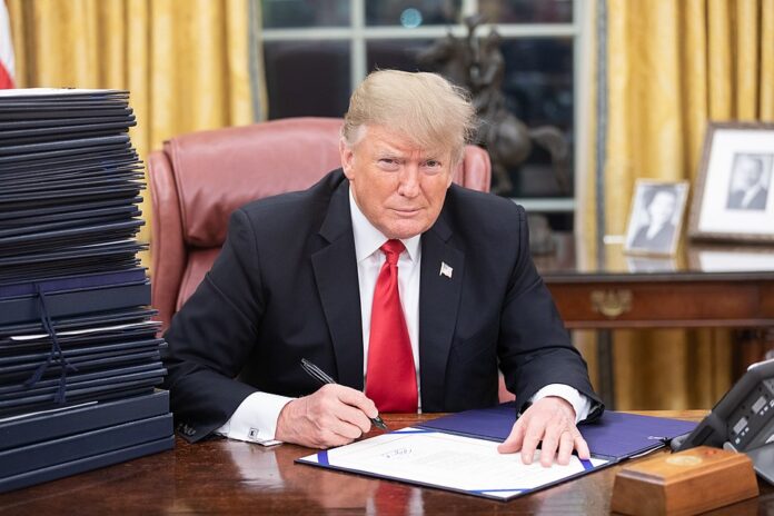 President Donald J. Trump is seen at his desk in the Oval Office with a stack of documents awaiting his signature. (Official White House Photo by Shealah Craighead)